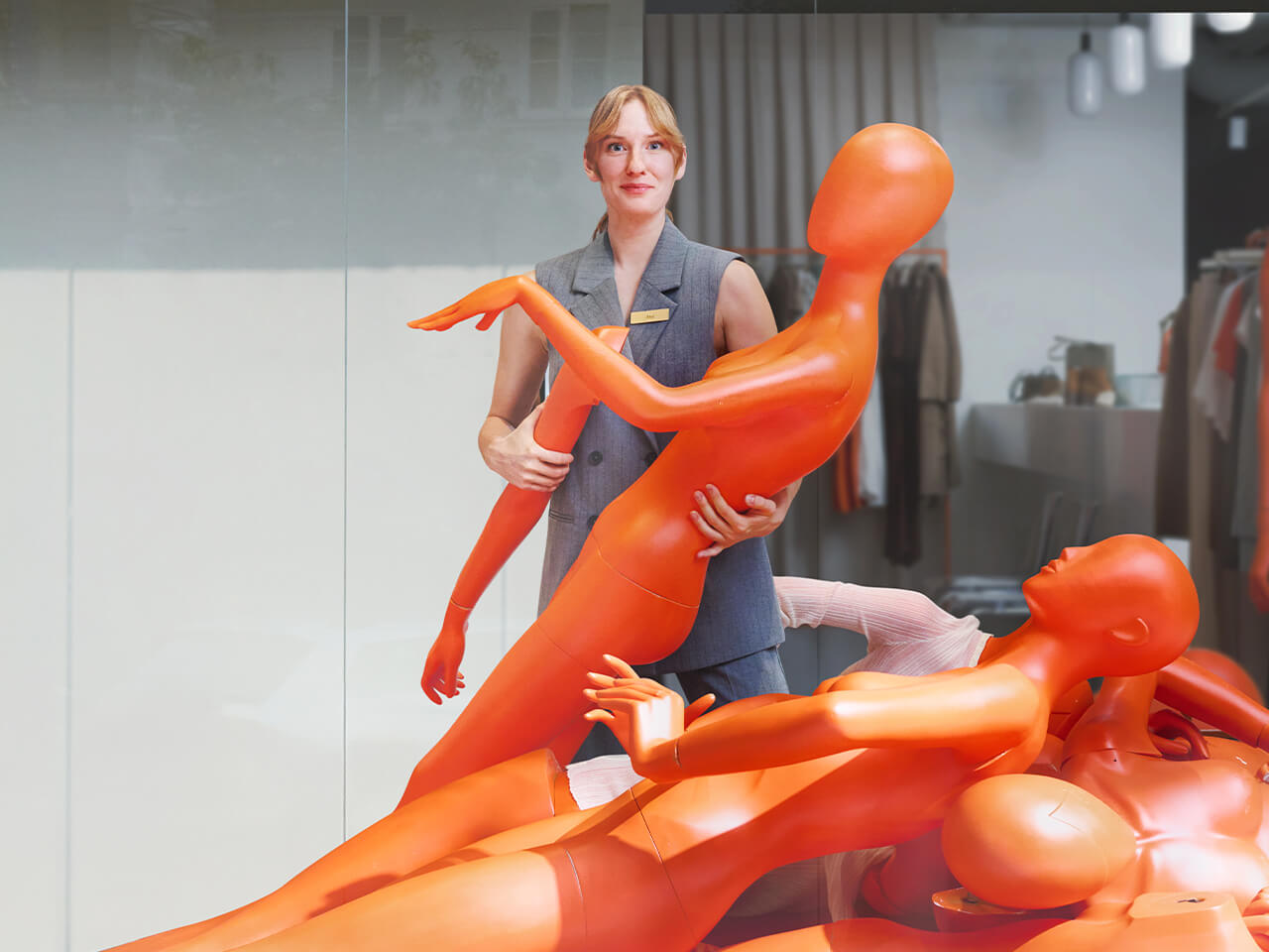 Naine seisab poes mitme langenud oranži mannekeeni vahel, hoides ühes käes mannekeeni ja teises mannekeeni kätt.